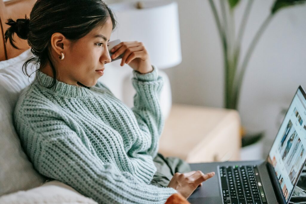 Woman shopping online on a laptop while holding a credit card, illustrating e-commerce and digital payments.