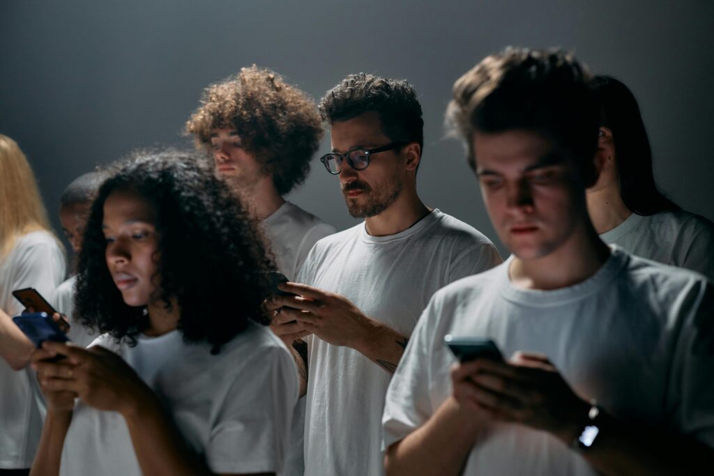 Group of young adults using smartphones indoors, focused on mobile screens and digital communication.